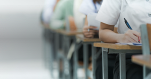 Estudantes em fileira de carteiras escrevendo a redação durante a prova