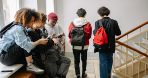 Grupo de jovens com mochilas no corredor da escola olhando o celular