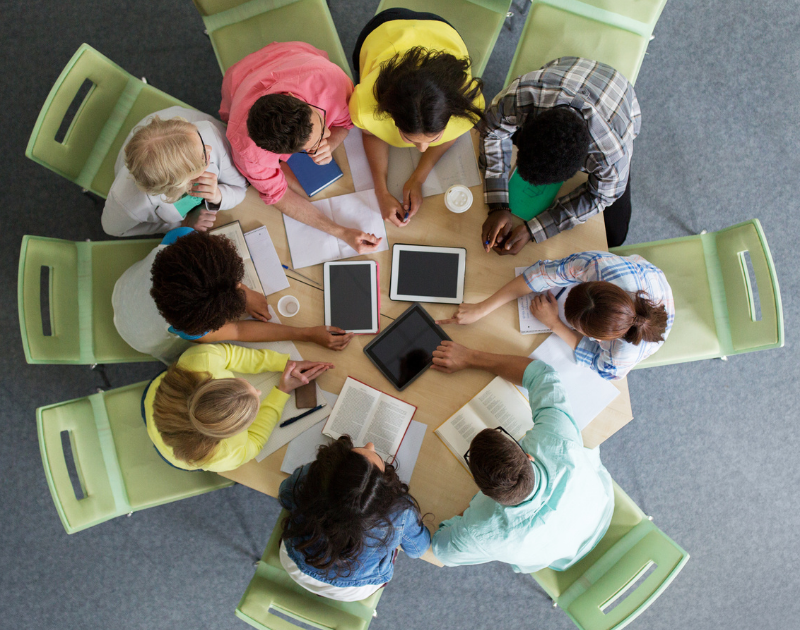 Vista de cima de estudantes em roda estudando com livros e tablets