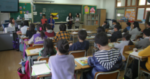 Sala de aula com estudantes em carteiras assistindo a uma apresentação
