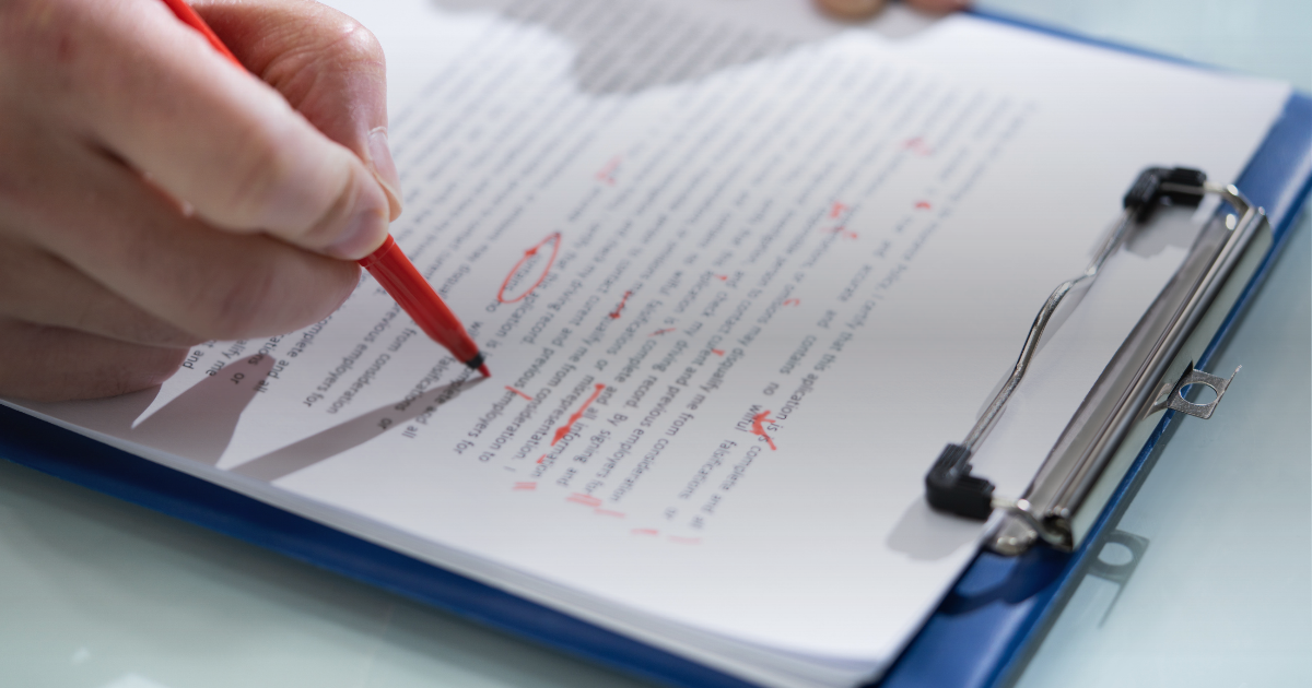 Mão com caneta vermelha corrigindo um texto em uma prancheta