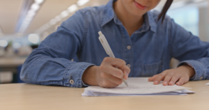 Estudante escrevendo a redação à mão em folha de papel sobre a mesa