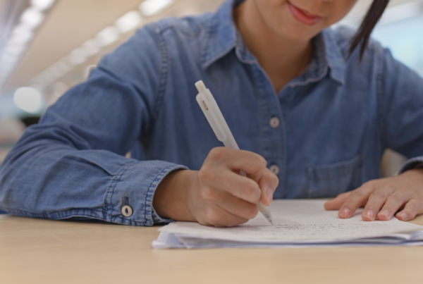 Estudante escrevendo a redação à mão em folha de papel sobre a mesa
