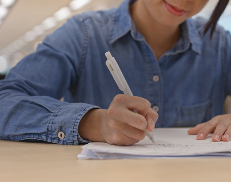 Estudante escrevendo a redação à mão em folha de papel sobre a mesa