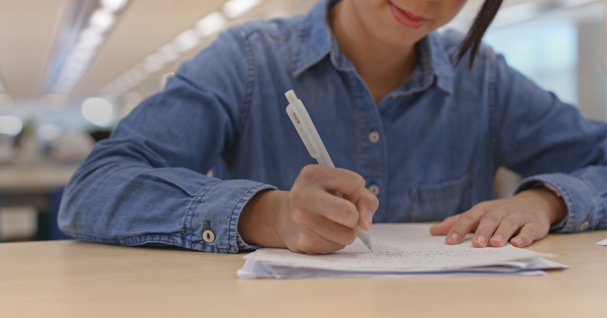 Estudante escrevendo a redação à mão em folha de papel sobre a mesa